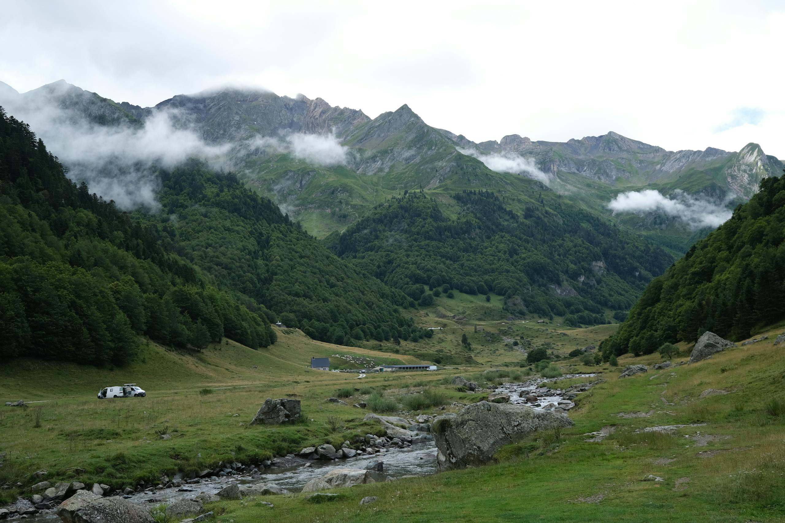 Breathtaking view of a lush mountain valley with fog hugging the peaks and a tranquil river flowing through.